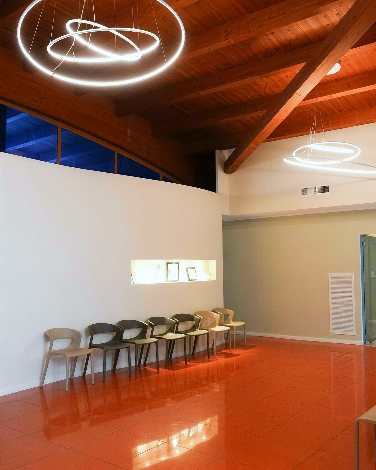 La sala d'attesa del centro, con il soffitto in legno, le luci ad anello, le sedute in fila e il pavimento color terracotta