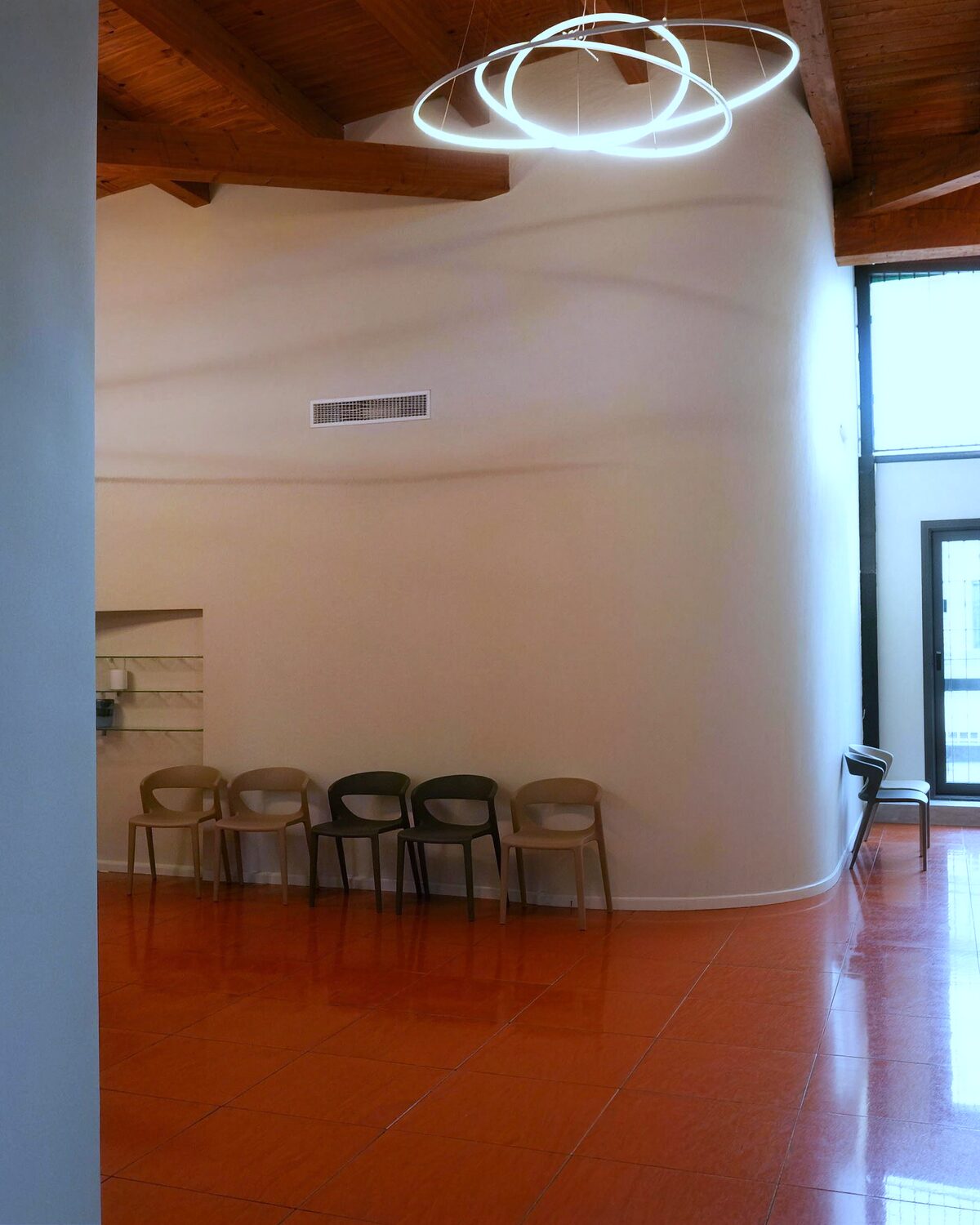 Un angolo della sala d'attesa: la parete curva, le sedute in fila, la luce ad anello sotto il soffitto in legno