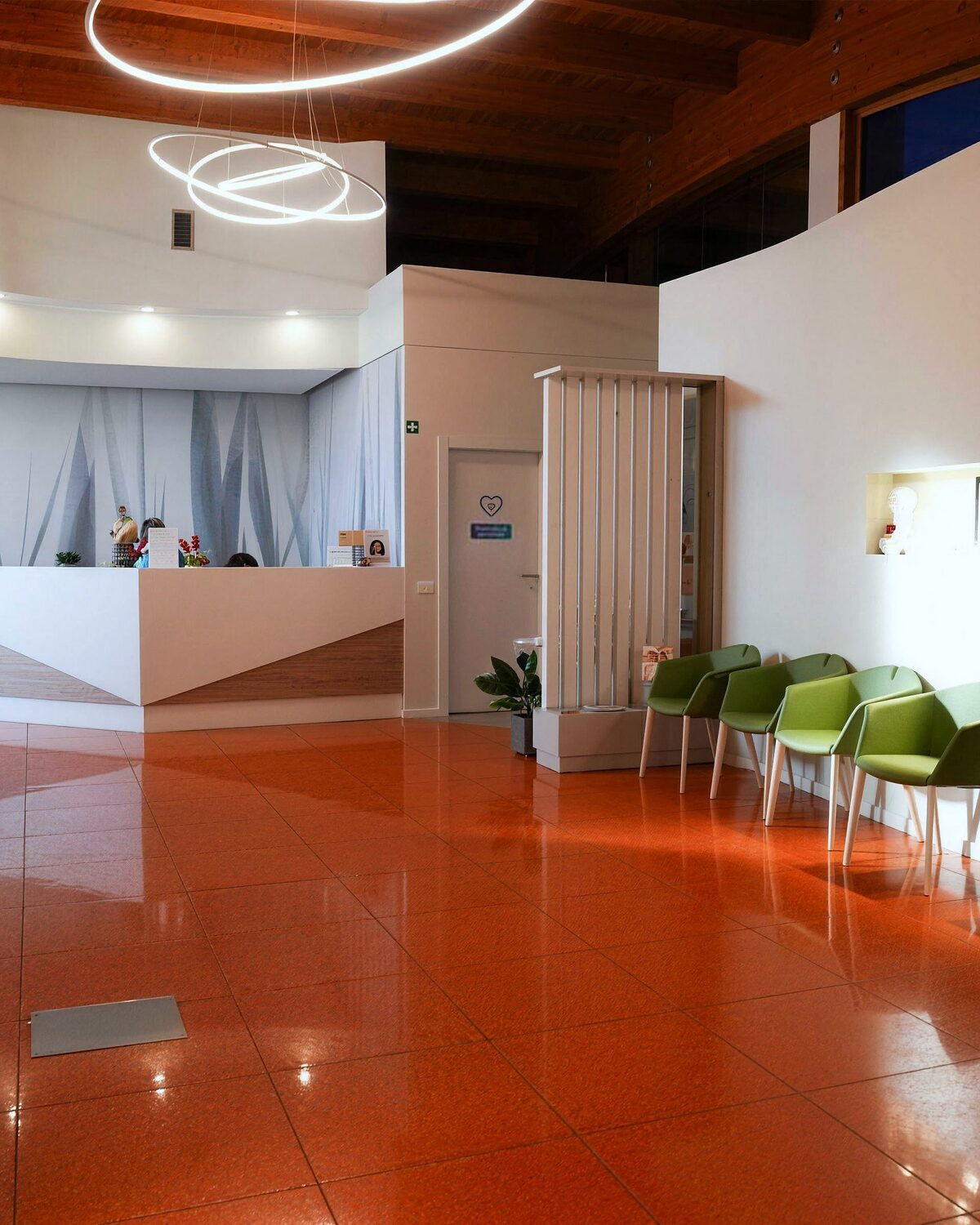 L'ingresso del Centro Medico Forma Sana: il bancone dell'accoglienza, le sedute verdi e il pavimento color terracotta sotto le luci ad anello